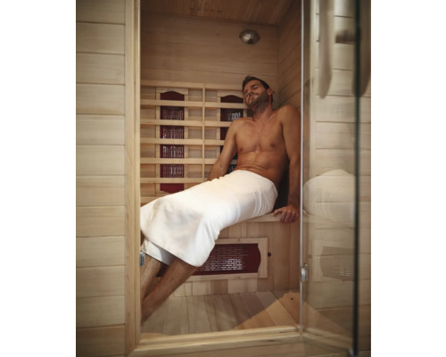 Muž relaxuje v infračervené sauně s dřevěnými stěnami a skleněnými dveřmi