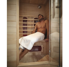 Muž relaxuje ve světlé dřevěné infra sauně se skleněnými dveřmi