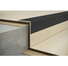 Detail schodové hrany s černým profilem na betonovém schodišti a laminátové podlaze.