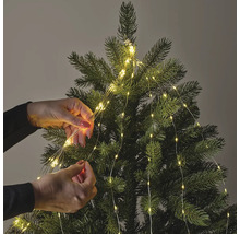 Osoba zdobí vánoční stromeček světelným řetězem.