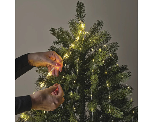 Osoba zdobí vánoční stromeček světelným řetězem.