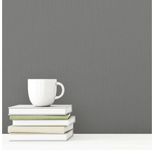 Šedá vliesová tapeta s textilní strukturou vedle šálku a knih