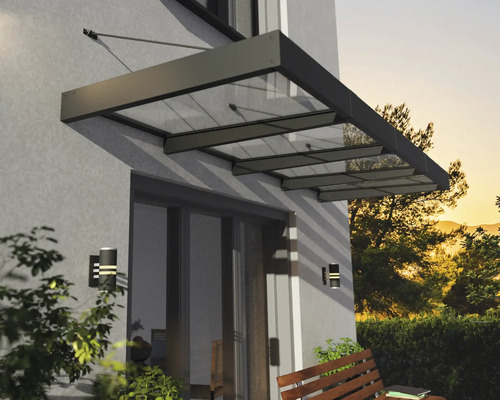 Moderní stříška ze skla a kovu nad terasovými dveřmi na stěně domu s nástěnnými svítidly a dřevěnou lavičkou.