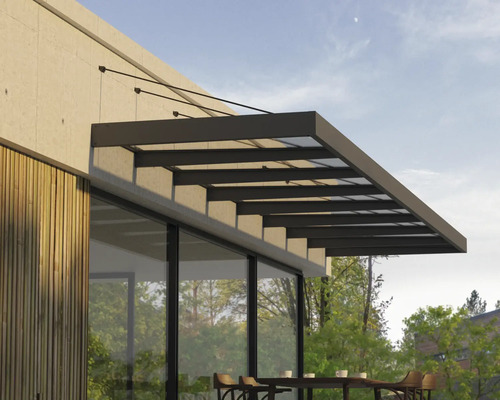 Moderní zastřešení terasy ze skla a tmavého kovu namontované na stěnu domu s dřevěným obkladem nad venkovním posezením.