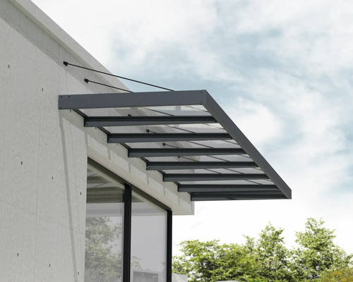 Moderní vchodová stříška ze skla s antracitovým hliníkovým rámem a lankovým zavěšením na světlé fasádě.