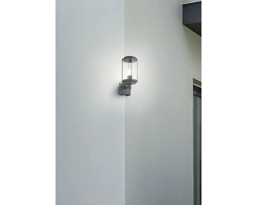 Šedé venkovní nástěnné svítidlo s čirým válcovým skleněným stínidlem osvětluje roh.
