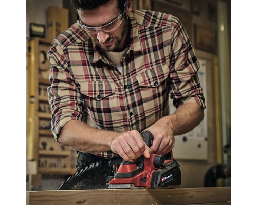 Muž hoblí dřevo elektrickým hoblíkem Einhell v dílně.