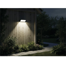 Venkovní pohled na dům se svítící nástěnnou lampou, obklopený rostlinami a chodníkem