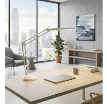 Světlá kancelář s psacím stolem, stolní lampou, notebookem, rostlinou a oknem s výhledem na město