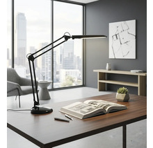 Stůl s lampou s otočným ramenem, knihou a pery ve světlé kanceláři.