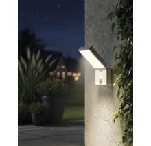 Osvětlený venkovní snímek s obdélníkovým nástěnným svítidlem se senzorem pohybu vedle rostlin.