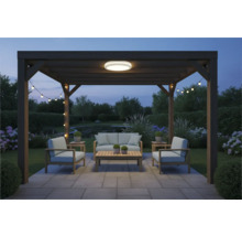 Pergola se zahradním nábytkem, stropním svítidlem a světelným řetězem na zahradě za soumraku.