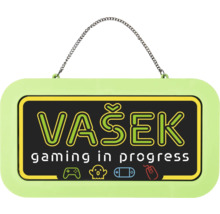 Světle zelená závěsná cedule s řetízkem, nápis VAŠEK gaming in progress a herní symboly.