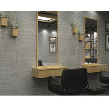 Moderní kadeřnictví se šedou stěnou v imitaci kamene, velkými zrcadly s dřevěným rámem, plovoucími dřevěnými policemi a černými kadeřnickými křesly.