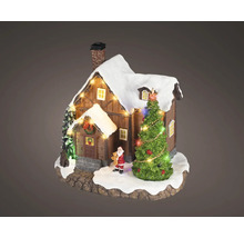 Miniaturní vánoční domeček ze dřeva se zasněženou střechou, osvětleným stromkem a malou figurkou Santa Clause.
