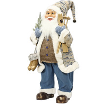 Figurka Santa Klause v zimním oblečení s lyžemi, hůlkami a bruslemi, v kabátě se vzorem, modrých kalhotách a čepici.
