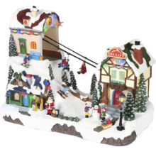LED osvětlená vánoční vesnička s pohyblivým lyžařským vlekem, zasněženými domy, jedlemi a figurkami jako je Santa Claus a lyžaři.