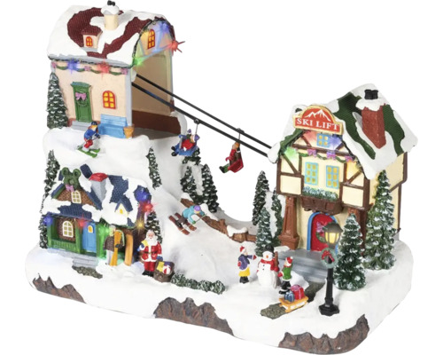 LED osvětlená vánoční vesnička s pohyblivým lyžařským vlekem, zasněženými domy, jedlemi a figurkami jako je Santa Claus a lyžaři.