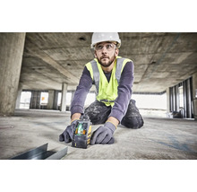 Řemeslník v ochranné přilbě a reflexní vestě používá na betonové stavbě křížový laser Dewalt pro přesné vyrovnání.