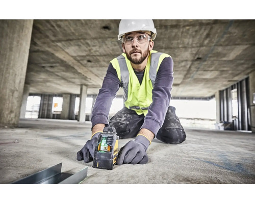 Řemeslník v ochranné přilbě a reflexní vestě používá na betonové stavbě křížový laser Dewalt pro přesné vyrovnání.