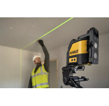 Stavební dělník v pracovním oděvu označuje stěnu pomocí křížového laseru DeWalt na stativu v interiéru.