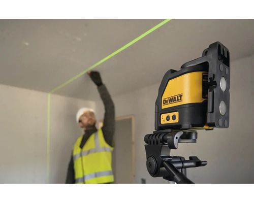 Stavební dělník v pracovním oděvu označuje stěnu pomocí křížového laseru DeWalt na stativu v interiéru.