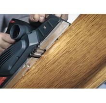 Elektrický hoblík při opracování dřevěného trámu, detailní záběr hoblování na hraně dřeva.