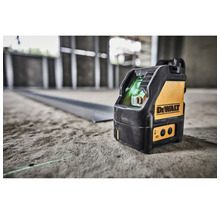 Křížový laser DeWalt na betonové podlaze na staveništi promítá zelenou laserovou linku na kovový profil