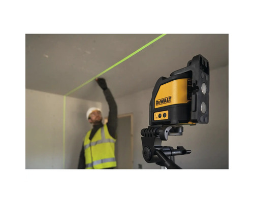 Stavební dělník v pracovním oděvu používá křížový laser DeWalt na stativu k přesnému zaměření zelené laserové linie na stěně.