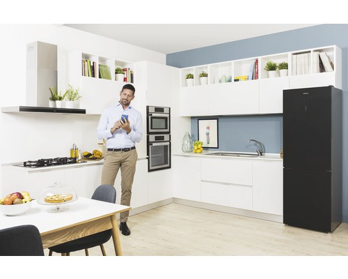 Světlá kuchyně s vestavěnými spotřebiči a osobou používající mobilní telefon.