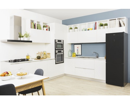 Světlá kuchyň s bílými skříňkami, černou lednicí a jídelním stolem.