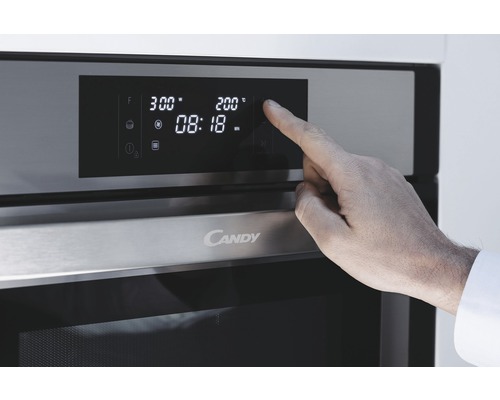 Detailní záběr trouby Candy s displejem a rukou provádějící nastavení.