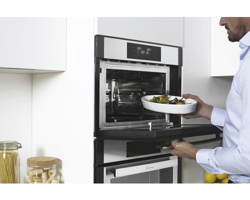 Muž zasouvá pekáč do trouby ve světlé kuchyni