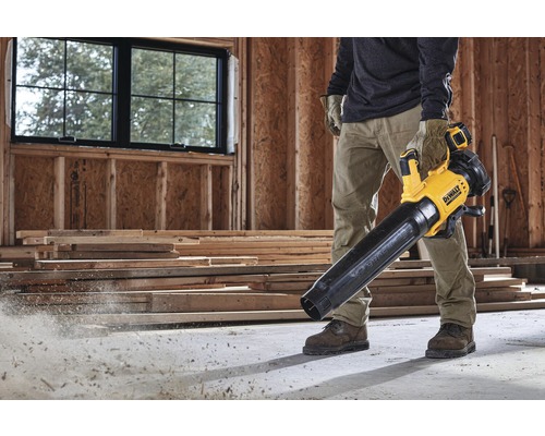 Muž používá žlutý a černý akumulátorový foukač listí DeWalt na staveništi.