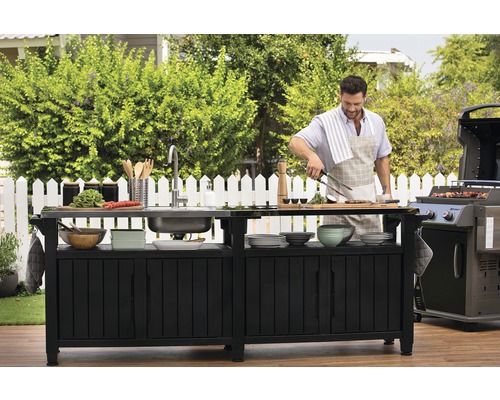 Venkovní kuchyně s dřezem, grilem a osobou, která připravuje jídlo