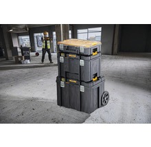 Stohovatelné boxy na nářadí s kolečky a stavební dělník v pozadí