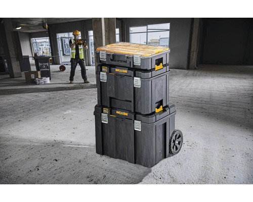 Stohovatelné boxy na nářadí s kolečky a stavební dělník v pozadí