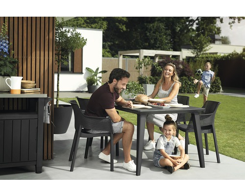 Rodina sedí venku u zahradního stolu se židlemi.