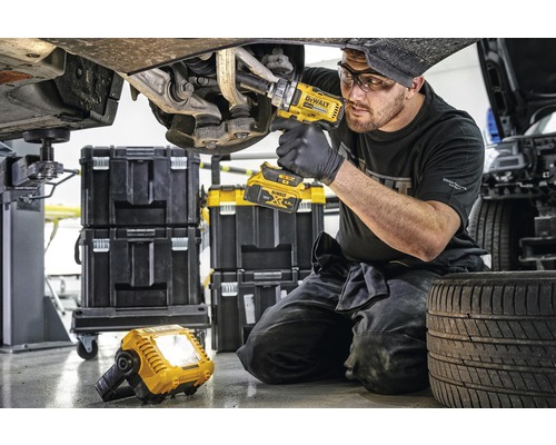 Mechanik pracuje s akumulátorovým rázovým utahovákem na autě, v pozadí kufříky na nářadí a pracovní lampa.