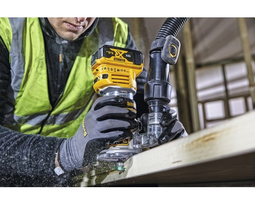 Muž frézuje dřevěnou desku akumulátorovou horní frézkou. Připojena je odsávací hadice. Značka: DeWalt