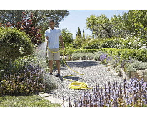 Muž zalévá rostliny zahradní hadicí v upravené zahradě.