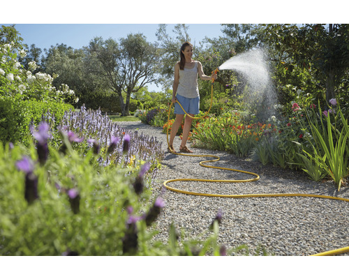 Žena zalévá rostliny na zahradě pomocí zahradní hadice