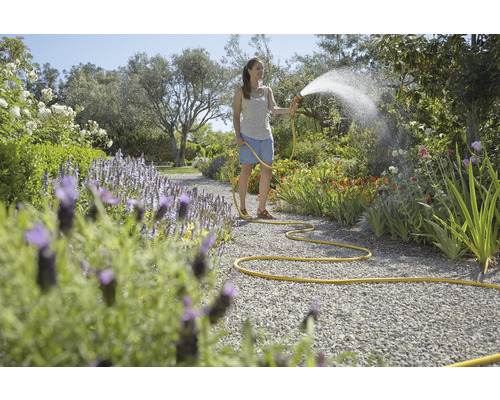 Žena zavlažuje zahradní cestu zahradní hadicí.