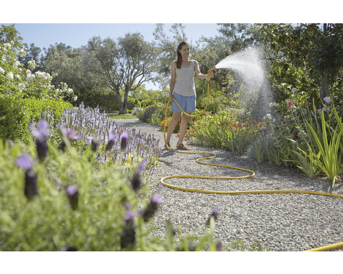 Žena zavlažuje zahradu zahradní hadicí a stříkací pistolí