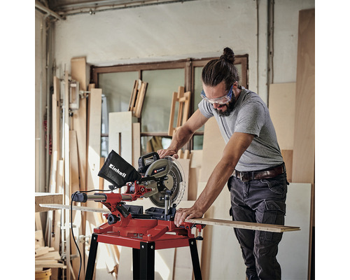 Muž používá pokosovou pilu Einhell k řezání dřevěné desky v dílně.