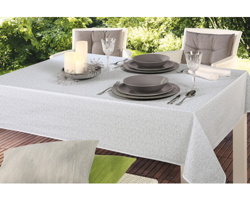 Prostřený zahradní stůl s bílým vzorovaným ubrusem, nádobím, sklenicemi a svíčkami