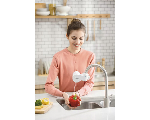 Žena myje papriky pod kohoutkem s vodním filtrem v kuchyni.