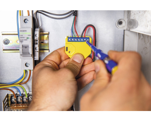 Elektrikář montuje elektronický komponent pomocí šroubováku do rozvodné skříně