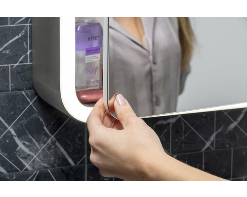 Žena otevírá zrcadlovou skříňku v koupelně