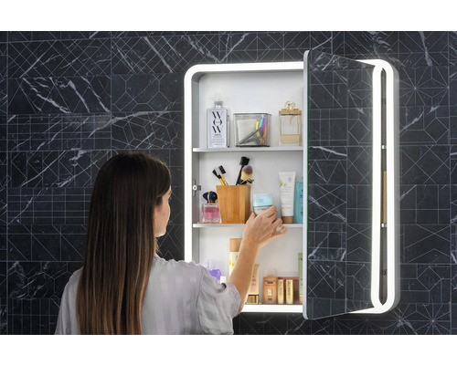 Žena před zrcadlovou skříňkou s osvětlením v koupelně